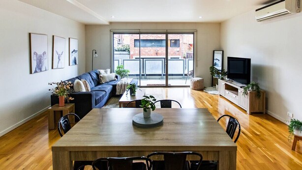A modern living room with a sofa, dining table, and TV. - Penny. 2BR Stylish Brunswick Stay w/ Parking (Brunswick)