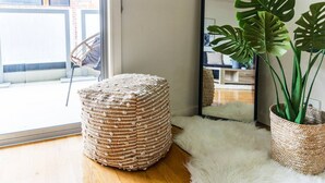 A room with a large mirror reflecting a living area, a wicker ottoman, and a potted monstera plant. - Penny. 2BR Stylish Brunswick Stay w/ Parking (Brunswick)