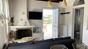 A modern living room with a fireplace, sofa, and dining area. - Helios Thalassa 82 sqm (Tinos)