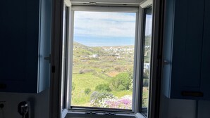 A room with a large window offering a view of a coastal landscape. - Helios Thalassa 82 sqm (Tinos)