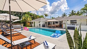Un jardin avec une piscine, des chaises longues, des parasols et un espace barbecue.