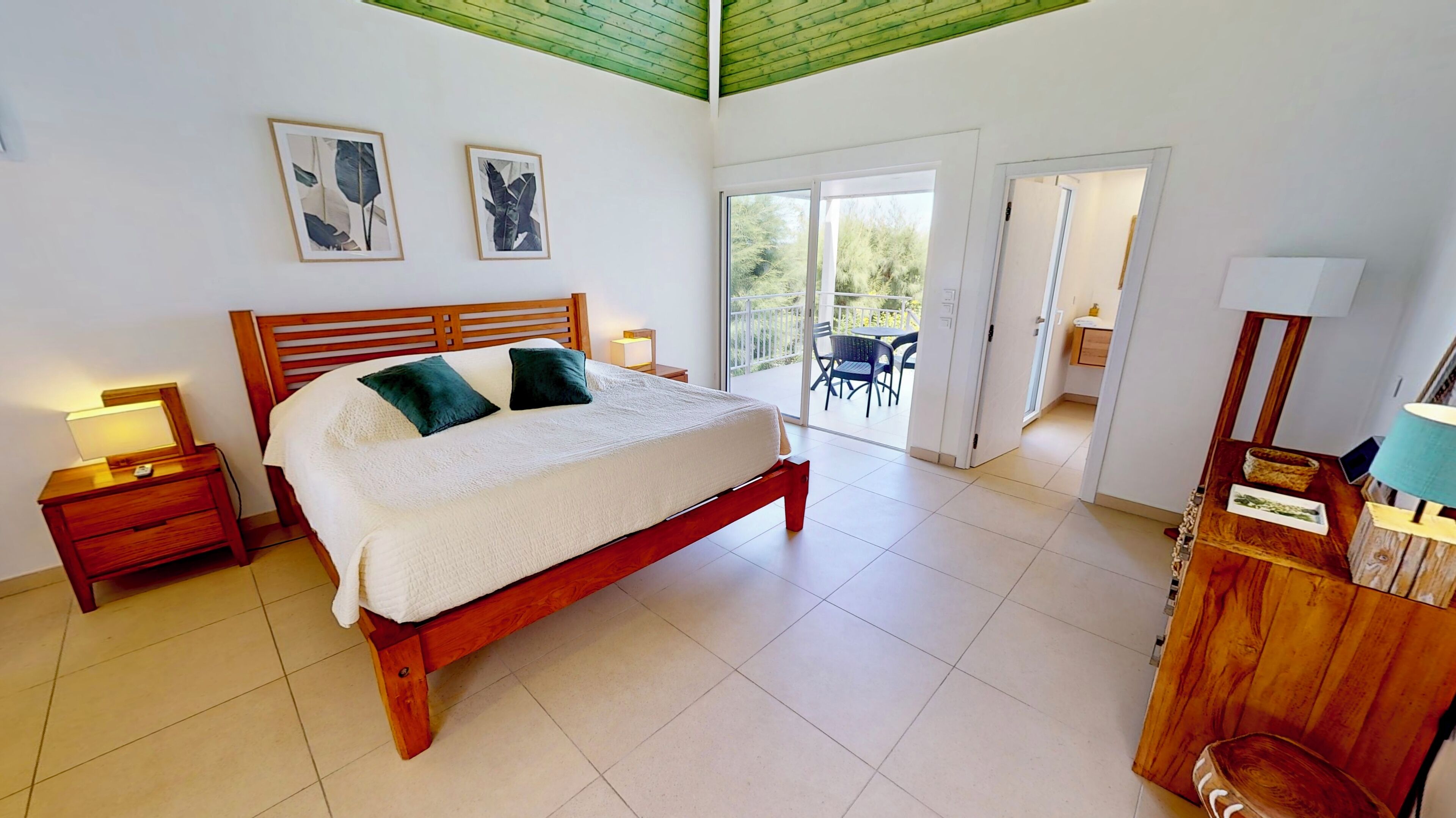 Une chambre avec un lit en bois, deux tables de chevet avec des lampes, un balcon avec une chaise et une vue sur la verdure.