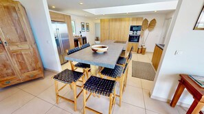 A modern kitchen with a central island, wooden cabinets, and a dining area with woven chairs.