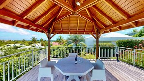 Un espace extérieur abrité, avec une table et des chaises, entouré d’une terrasse en bois et de rampes blanches.