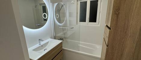 A modern bathroom with a glass-enclosed shower, a large mirror with circular lights, and a wooden vanity.