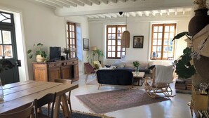 A spacious living area with a dining table, chairs, a sofa, and a rocking chair. There are potted plants, a television, and a bookshelf. - La Thibaude - Vigeronne house near Lyon (Charly)