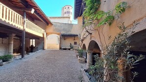 A cobblestone courtyard with a wooden balcony, stone pillars, and a rustic building with an arched entrance. - La Thibaude - Vigeronne house near Lyon (Charly)