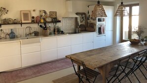 A kitchen with a central island, white cabinetry, hanging wicker light fixtures, and a large wooden table with chairs. - La Thibaude - Vigeronne house near Lyon (Charly)