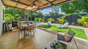 Un espacio al aire libre techado con piscina, sillas de descanso y una mesa de comedor.