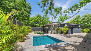 Una casa moderna con piscina, rodeada de abundante vegetación y palmeras.