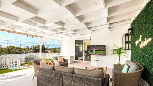 A covered outdoor seating area with wicker furniture, a pool, and a green wall with a neon sign. - Pool house w/Playground, Mini Golf, King Bed (Chula Vista)