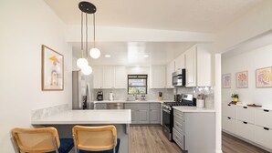 A modern kitchen with white cabinets, a central island with bar stools, stainless steel appliances, and pendant lighting. - Pool house w/Playground, Mini Golf, King Bed (Chula Vista)