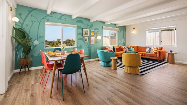 A spacious living room with a dining area, featuring a large plant, colorful furniture, and a view through the windows. - Pool house w/Playground, Mini Golf, King Bed (Chula Vista)