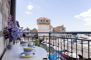 A balcony with a table set for tea, overlooking a historic tower and a marina. - A Apartment Near Beach With two Balconies (Kastela)