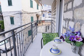 A balcony with a table set for two, a vase with flowers, and a view of the street below. - A Apartment Near Beach With two Balconies (Kastela)