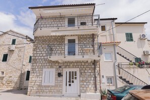 A two-story stone building with a balcony, a door, and a small window. - A Apartment Near Beach With two Balconies (Kastela)