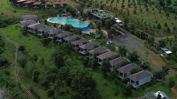 An aerial view of a resort with multiple bungalow-style buildings, a swimming pool, and lush green surroundings. - HIDDEN LEAF RESORT (Veal Veaeng)