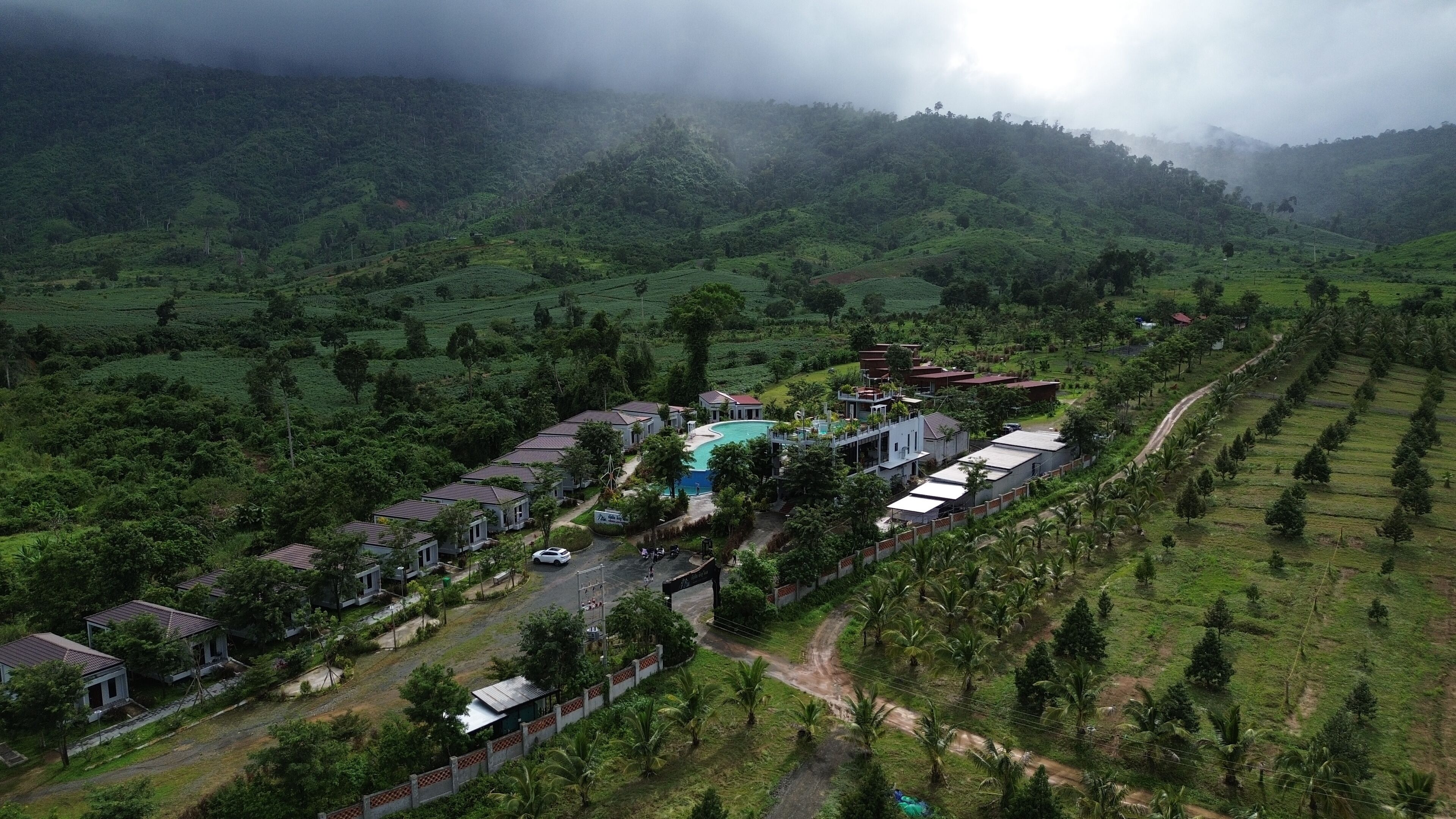 An aerial view of a resort with multiple buildings, a swimming pool, and lush green surroundings.