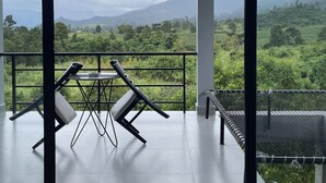 A balcony with a table and chairs, a hammock, and a view of a green landscape with mountains. - HIDDEN LEAF RESORT (Veal Veaeng)