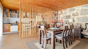 Eine Holzbalkendecke, ein Esstisch mit Stühlen, eine Küchenzeile und eine Steinwand mit Tellern.