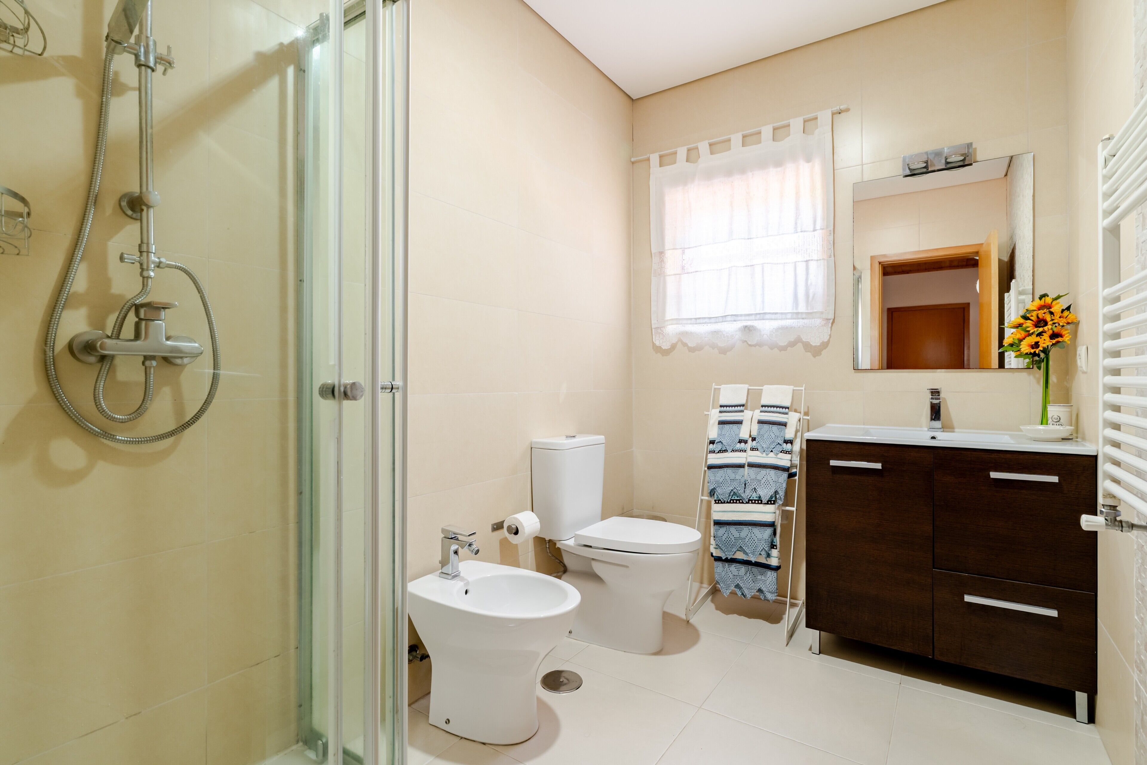 A bathroom with a glass shower enclosure, a toilet, a bidet, a sink, and a vanity with drawers.