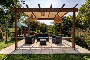 Un patio al aire libre con una pérgola de madera, muebles de mimbre y un colgante luminoso.