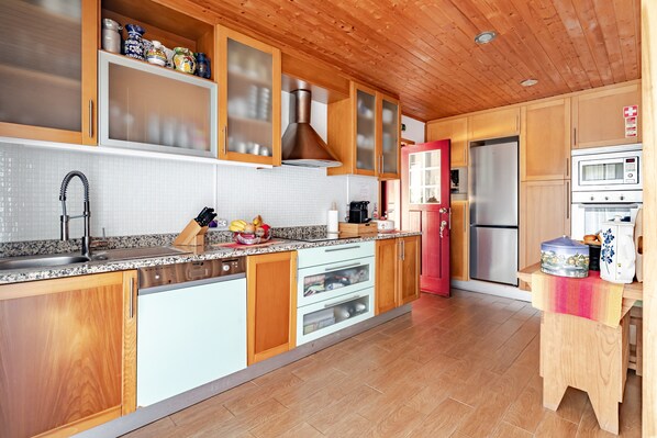 A modern kitchen with wooden cabinets, a stainless steel refrigerator, a microwave, and a wooden stool.