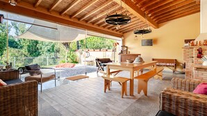 Eine großzügige Terrasse mit Korbmöbeln, einem Holztisch und einem Kamin aus Ziegeln.