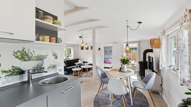 Eine moderne Küche mit Kochinsel, ein Essbereich mit rundem Tisch und Stühlen sowie ein gemütlicher Wohnbereich mit Sofa und Kamin.