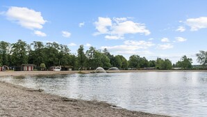 Ein Seeufer mit Sandstrand, einer kleinen Anlegestelle und einer Reihe von Ferienhäusern.