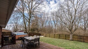 Eine Holzterrasse mit Tisch und Stühlen, einem Whirlpool und einem umzäunten Garten mit Bäumen.