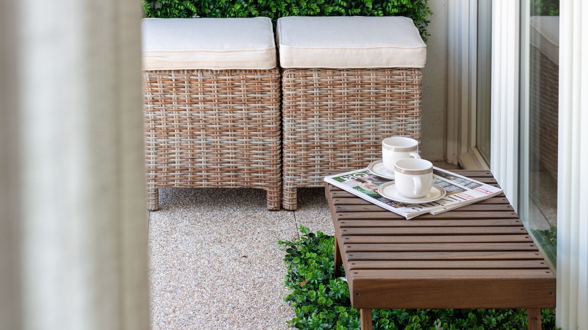 A wicker bench with cushions, a wooden table with a newspaper, and a glass door.