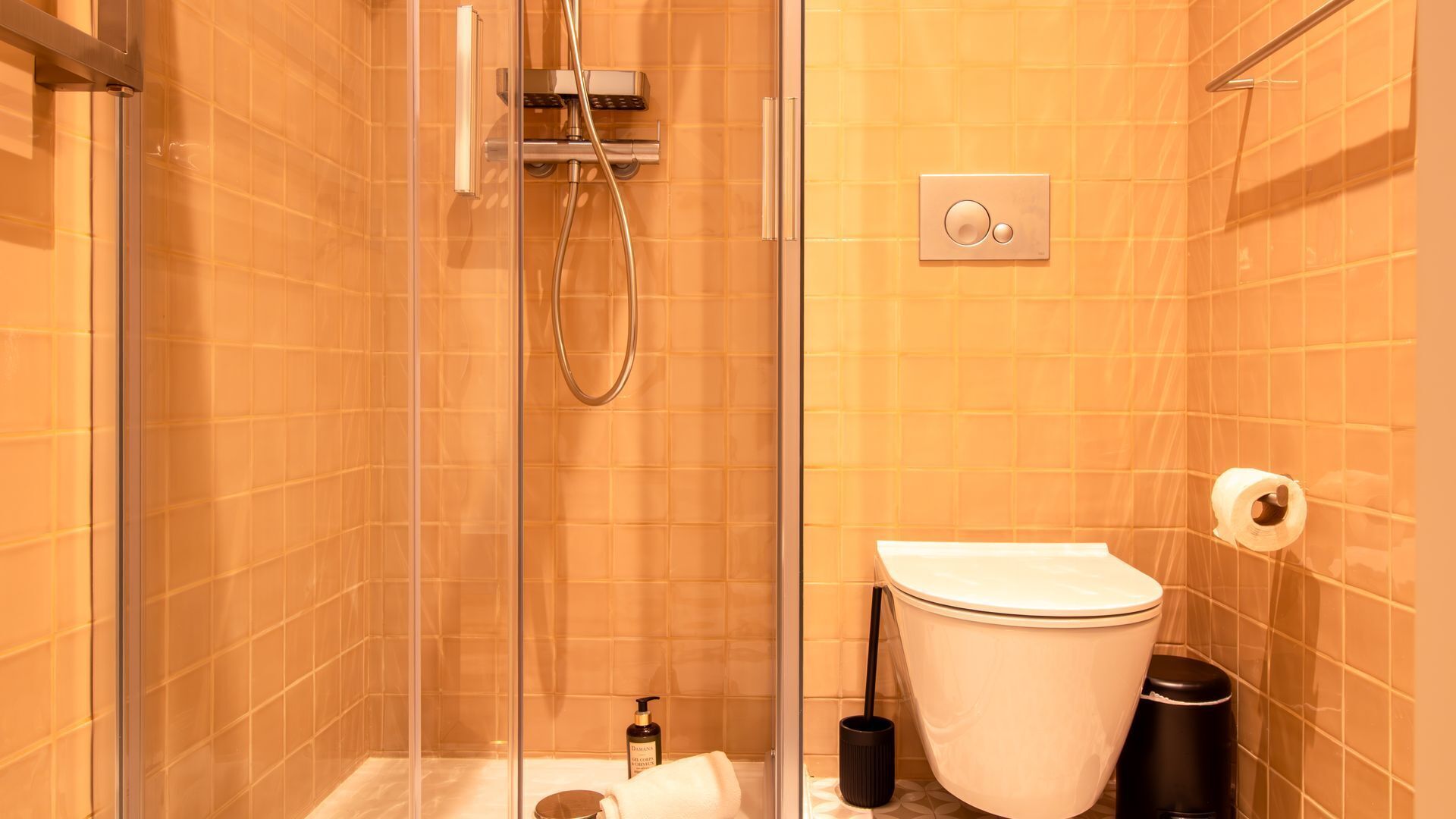 A modern bathroom with a glass shower enclosure, a toilet, and a trash bin.