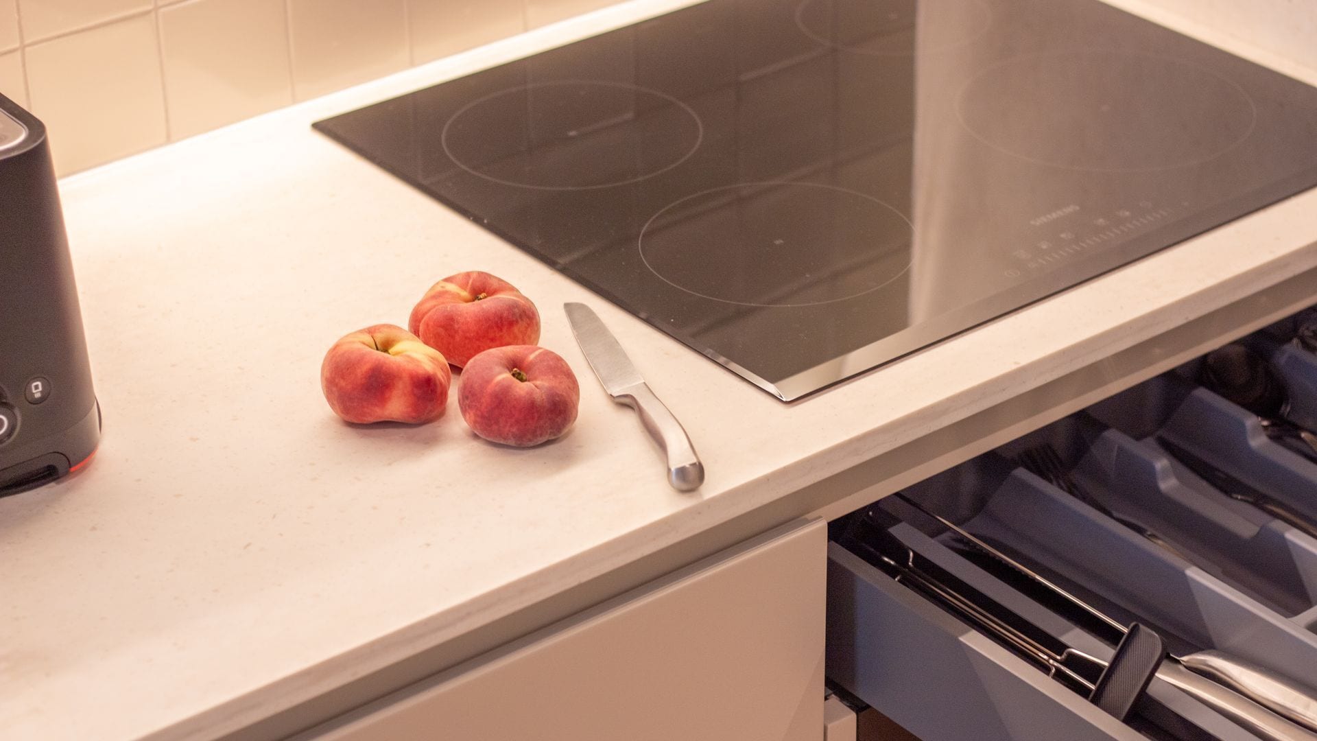 Un comptoir de cuisine avec une cuisinière, trois pêches et un couteau.