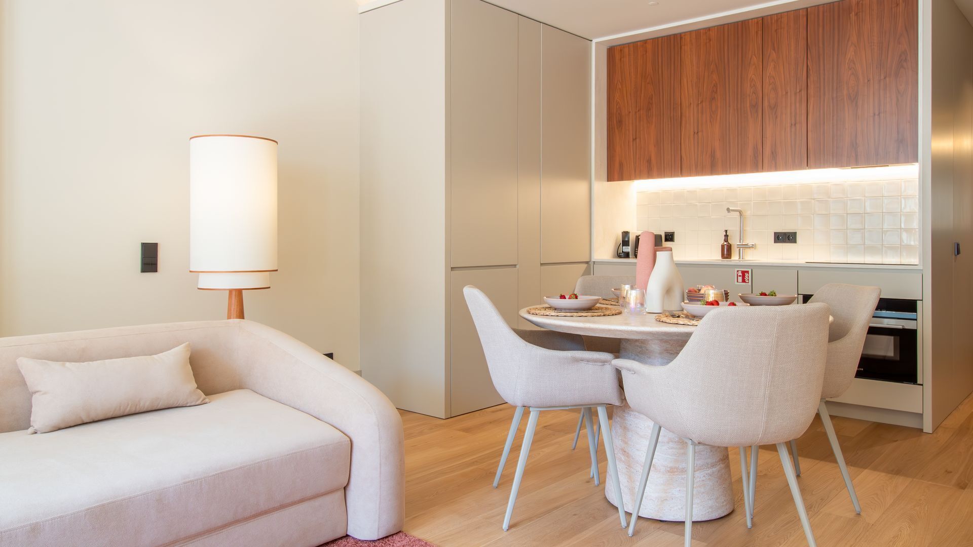 Een moderne woonkamer met een bank, een eettafel met stoelen en een keuken met houten kasten en een betegelde achterwand.
