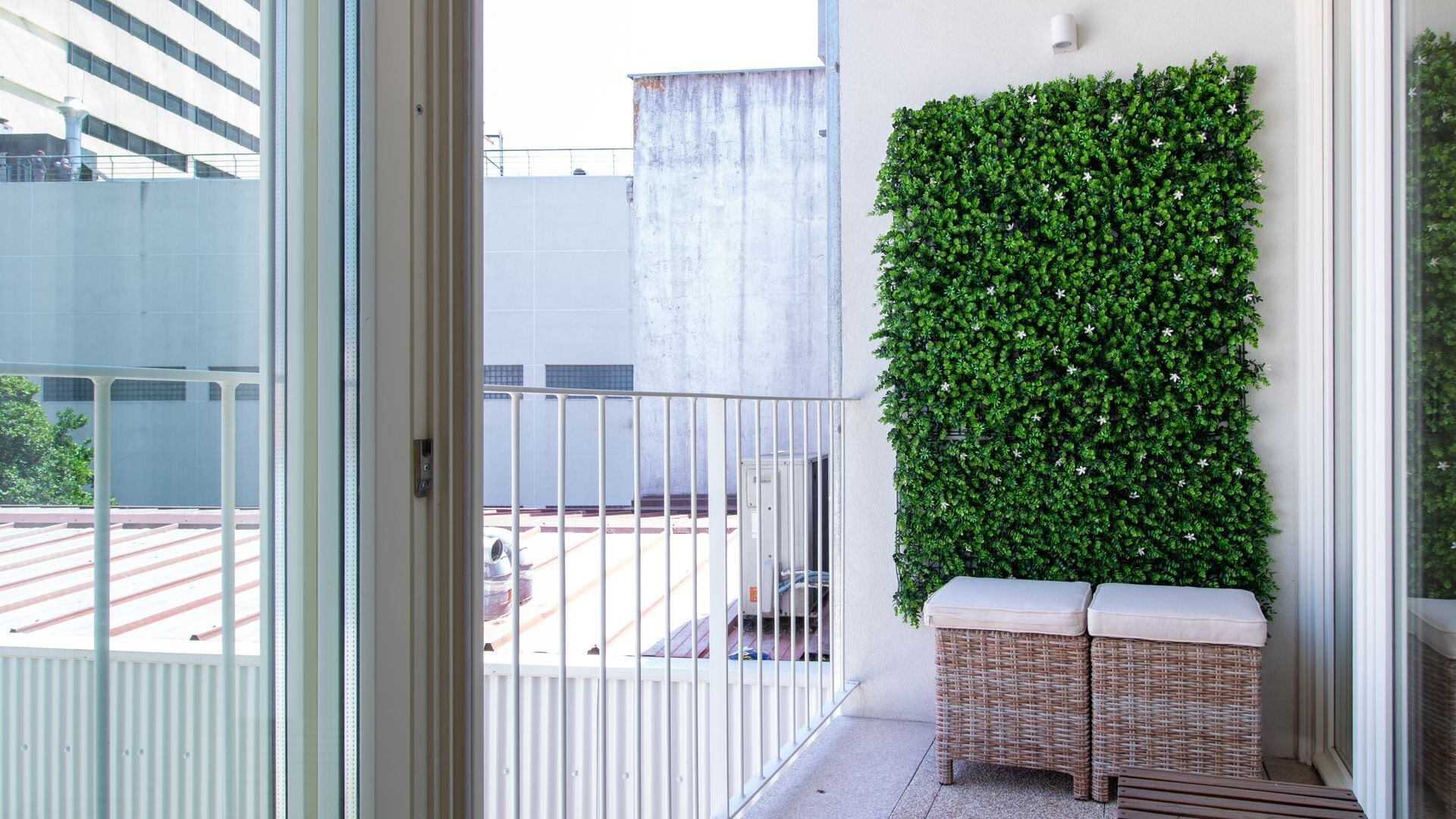 Ein Balkon mit weißer Brüstung, einem vertikalen Grünpflanzenwand und Korbmöbeln mit Kissen.