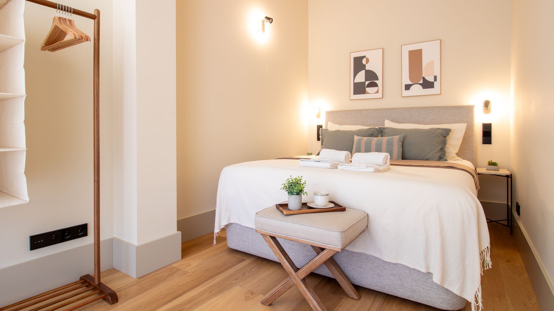 A neatly arranged bedroom with a bed, bedside tables, a hanging wardrobe, and wall-mounted artwork.