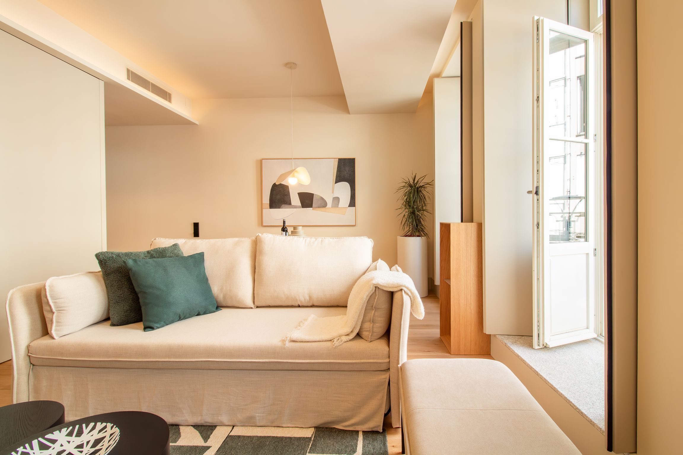 A modern living room with a sofa, a coffee table, and a side table. There is a painting on the wall and a plant in the corner.