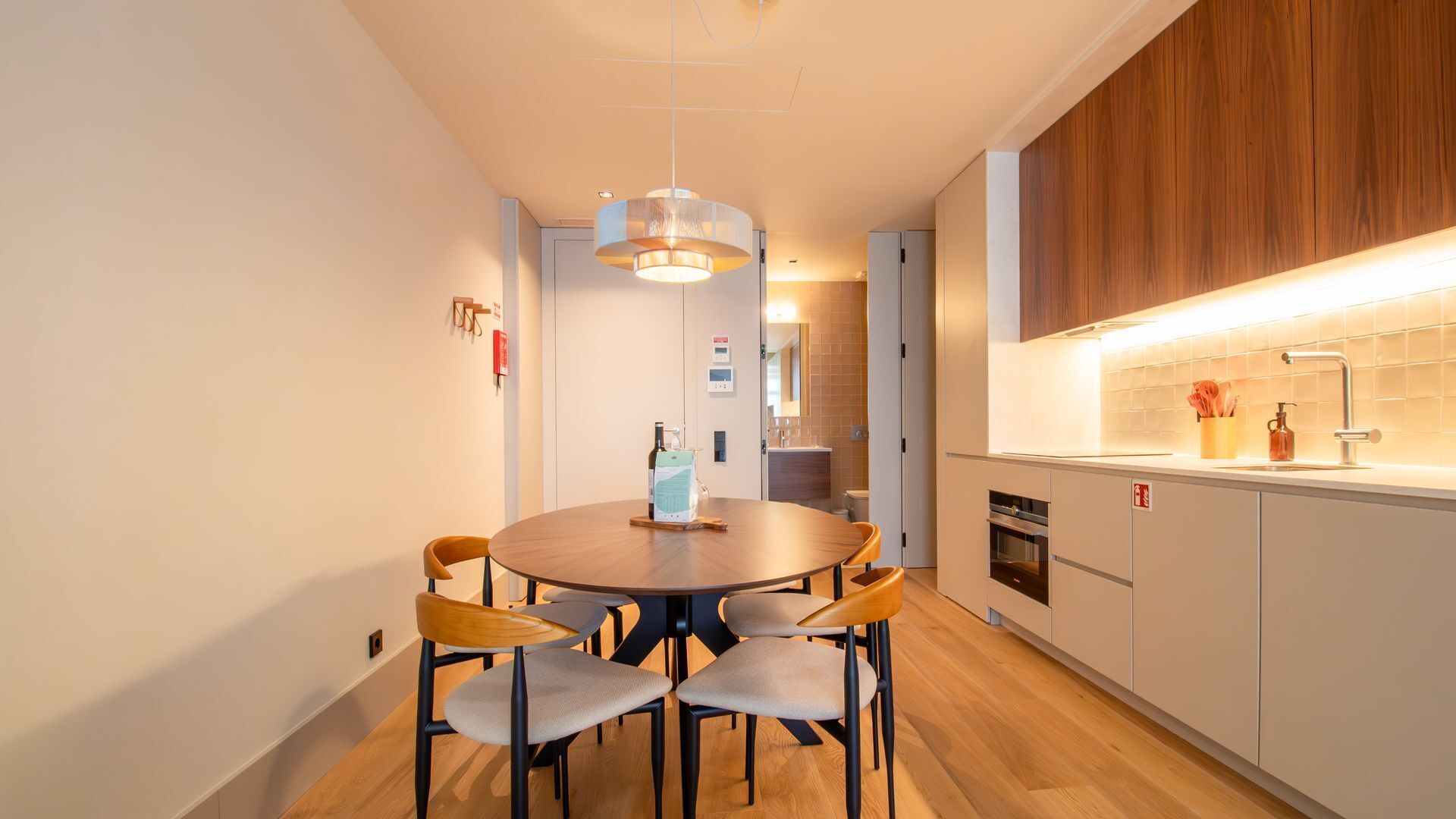 A modern kitchen with a round dining table and chairs, wooden cabinets, and a built-in oven.