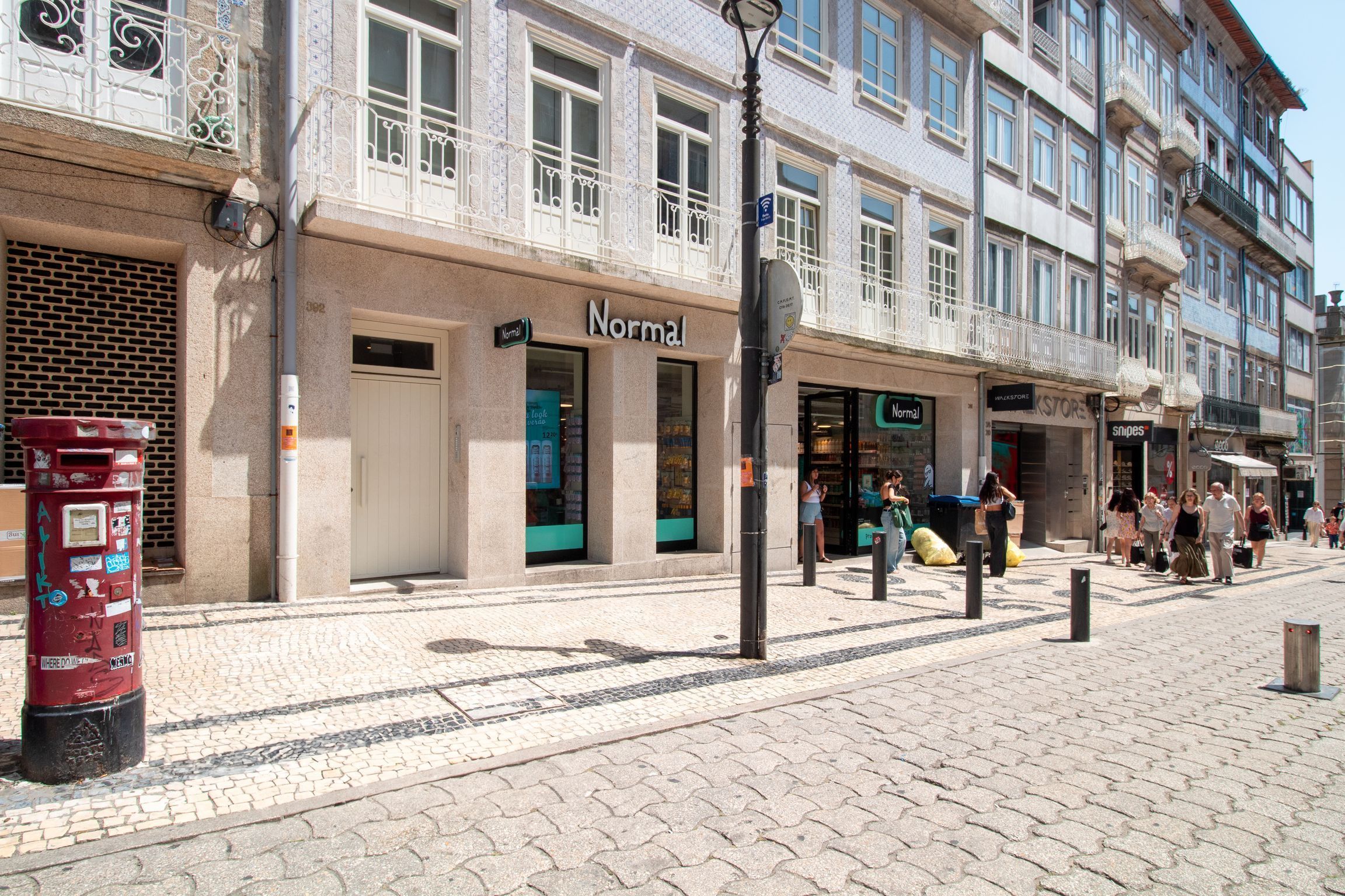 Una calle con una hilera de tiendas, incluyendo una tienda 'Normal' con escaparate verde.