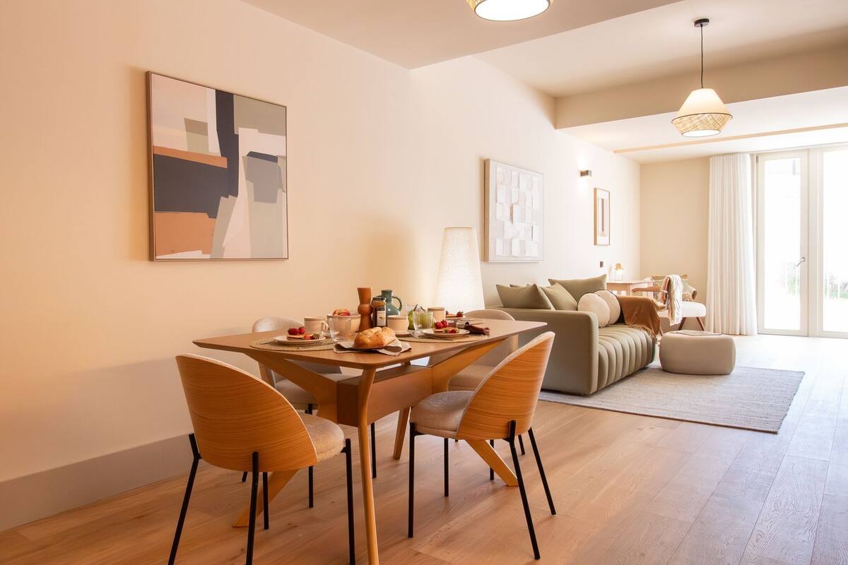 A modern dining area with a wooden table and chairs, a breakfast setup, and a living area with a sofa and cushions.