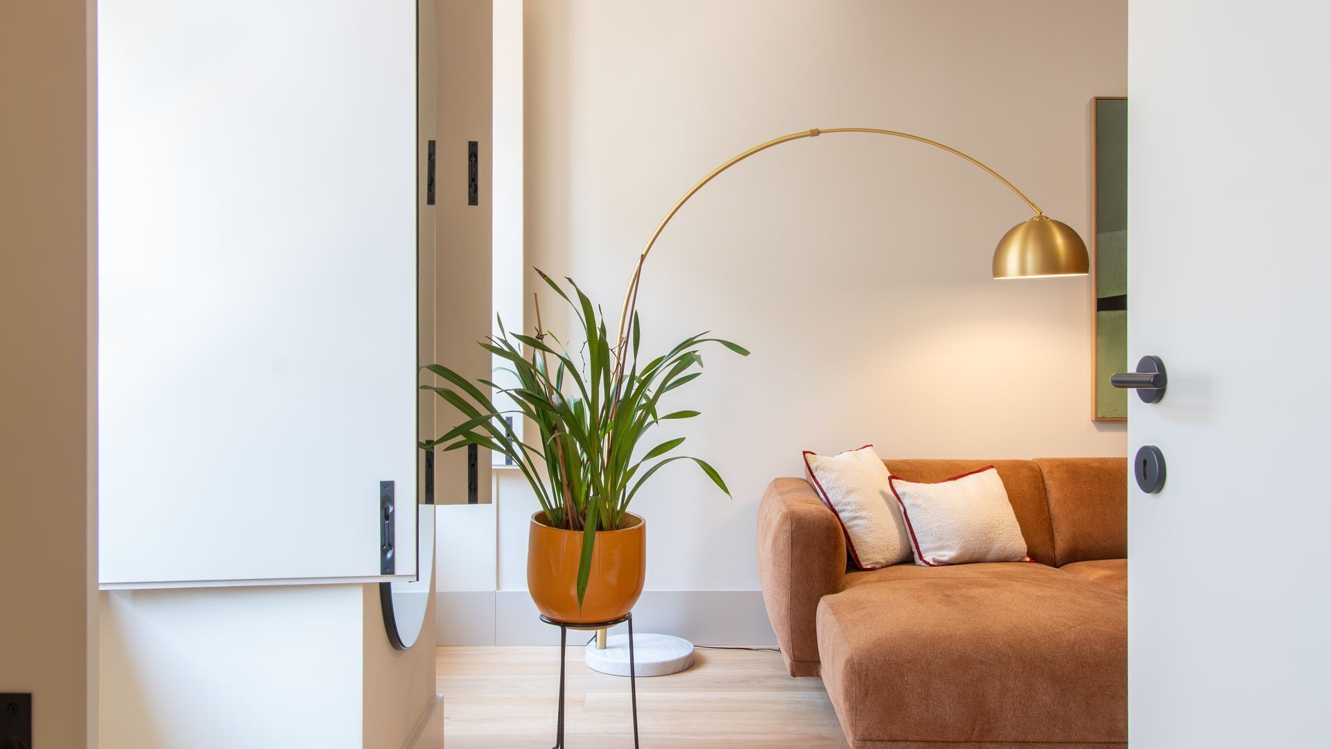 Uma sala de estar moderna com um sofá castanho, um vaso de planta e um abajur.