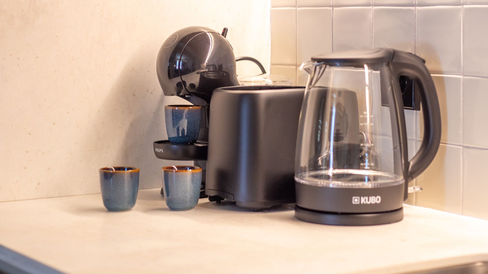 A coffee maker, a toaster, and two cups on a kitchen counter.