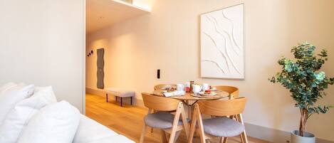 A modern hotel room with a wooden dining table set for breakfast, a bench, and a potted plant.