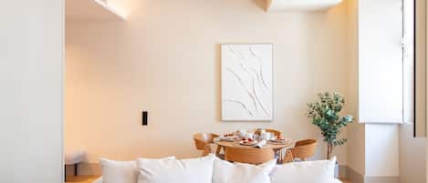 Una sala de estar moderna con un sofá, una mesa de comedor con sillas, una obra de arte abstracta colgada en la pared y una planta en maceta.