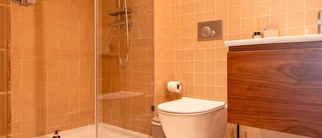 Un bany modern amb dutxa tancada per vidre, un vàter blanc i un tocador de fusta.