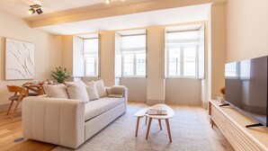 Ein modernes Wohnzimmer mit einer Couch, einem Couchtisch, einem Fernseher und großen Fenstern.