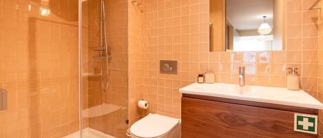 A bathroom with a glass-enclosed shower, a toilet, a sink with a mirror, and a wooden vanity.