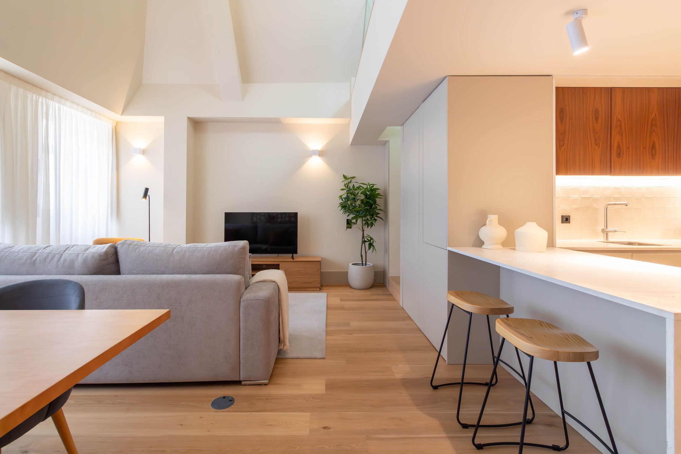 A modern living room with a sofa, a TV, and a dining area with a table and chairs.