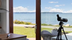 A room with a large window overlooking a lake, a tripod with a camera, and a wooden table.
